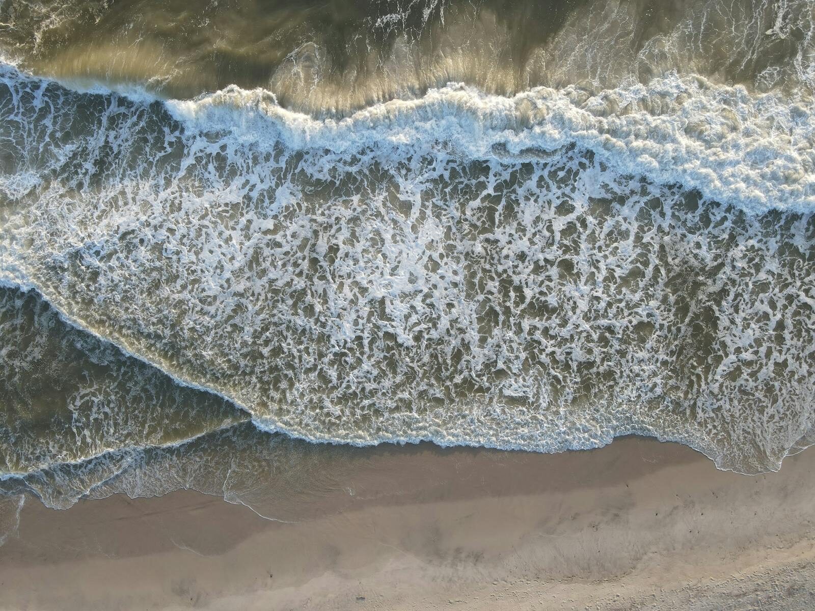Stunning aerial view of ocean waves crashing onto the sandy shores of Hvide Sande, Denmark.